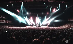 A wide shot of a concert with bright stage lights illuminating a large crowd.