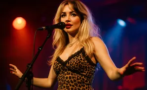 A blonde singer in a leopard print dress performs into a microphone under stage lights.