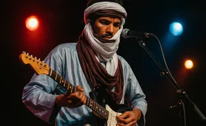 A man in traditional clothing plays an electric guitar on stage with stage lights.