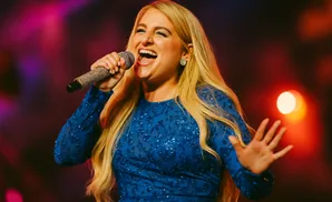 Singer Meghan Trainor performs on stage in a blue sequined dress, holding a microphone.