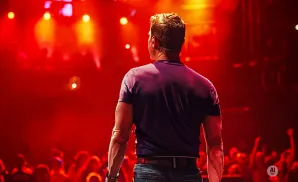 A man sings and plays an acoustic guitar on stage with blue spotlights.