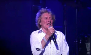 rod stewert performing on stage wearing a white shirt and diamond bracelet