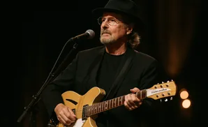 A man in a hat and suit plays a guitar and sings into a microphone.