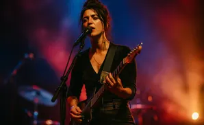 A female guitarist sings into a microphone while playing a guitar on stage.