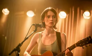 A woman plays an acoustic guitar on stage, bathed in warm spotlight.