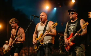 Three men playing bass guitars on stage with lights in the background.