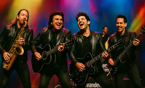 Four men in black leather jackets performing on stage. One plays the saxophone, two play guitars, and one plays the bass.