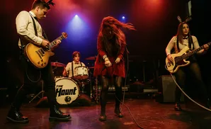 A rock band performs on stage with a guitarist, singer, bassist, and drummer.