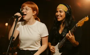 Two women performing music: one singing into a microphone and the other playing guitar.