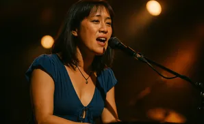 A woman in a blue dress sings into a microphone on a dimly lit stage.