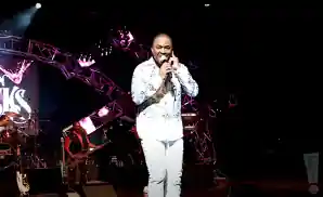 A lead singer in a white patterned shirt and pants performs on stage with a band.