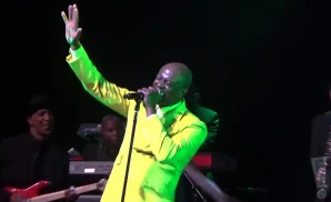 Singer in a yellow suit with his arm raised, singing into a microphone on stage.