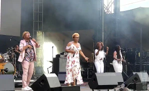 A band performs on stage, with singers in front and drums in the back.