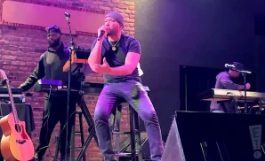 A singer performs on stage with a keyboard player and a guitarist.