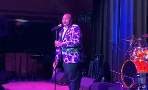 Singer on stage with a patterned jacket and microphone. Drum set visible on the right.