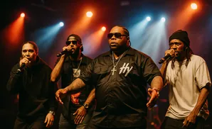 Four rappers perform on stage with microphones, illuminated by stage lights.