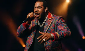 Rapper Busta Rhymes performs onstage wearing a colorful, patterned jacket and a diamond chain.
