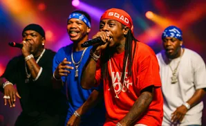 Four men performing on stage, three wearing bandanas, one with a red bandana and red shirt.