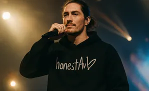 A man with dark hair pulled back, wearing a black hoodie with 
