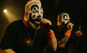 Two men with clown makeup performing on stage, one in focus singing into a microphone.