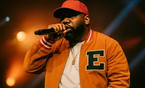 Rapper wearing a red cap and orange jacket with an 