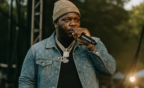 Rapper performing on stage wearing a denim jacket and a beanie, holding a microphone.