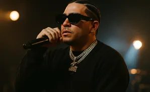 A man in sunglasses and chains sings into a microphone on a dimly lit stage.