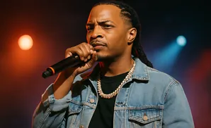 Rapper T.I. performs on stage wearing a denim jacket and gold chain, holding a microphone.