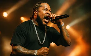 Rapper Xzibit performs on stage with a microphone, wearing a black t-shirt and diamond necklaces.