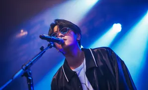 Singer in sunglasses performs on stage, bathed in blue and white spotlights.