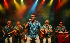 A band performs on stage, with a lead singer in a blue floral shirt holding a microphone and other band members playing instruments.