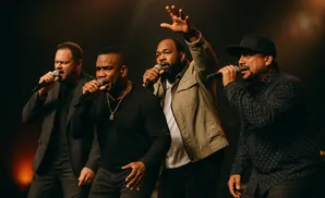 Four men singing into microphones on a stage.