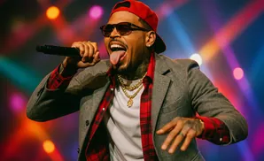 A male singer in a red hat, sunglasses, and gray blazer performs onstage, sticking his tongue out.