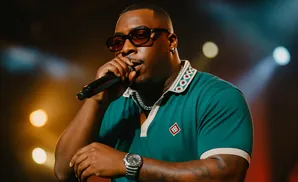 Man in a green polo shirt and sunglasses sings into a microphone on stage.