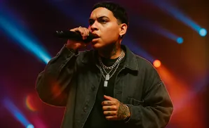 Rapper speaking into a microphone on a stage with blue and pink lights.