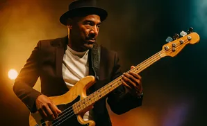 Man in a hat and suit plays a bass guitar on a dimly lit stage.