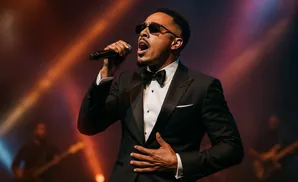 Singer in a black tuxedo and sunglasses performs with a microphone on stage.