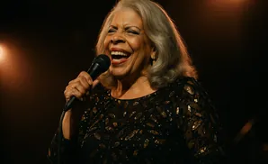 A woman with gray hair and a sparkling dress sings into a microphone.