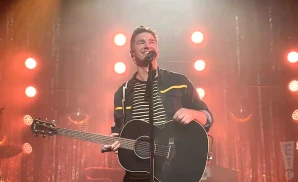 andy grammer playing the guitar live in front of red lights