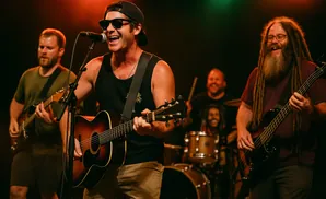 A band performs on stage with the lead singer playing guitar and singing into a microphone, flanked by other musicians.