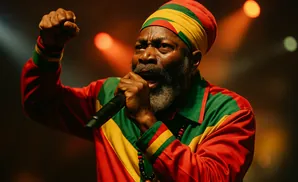 A Black man in a Rasta hat and colorful shirt performs into a microphone, fist raised.