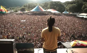 A musician with dreadlocks faces a huge crowd at an outdoor festival.