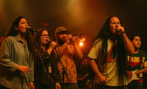 A band performs on stage, with singers at microphones and a trumpeter.