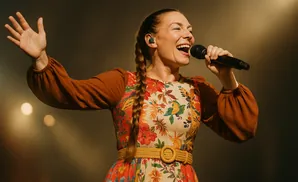 Singer performing on stage, wearing a floral dress and holding a microphone.