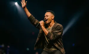 A man sings into a microphone with his arm raised in a concert.