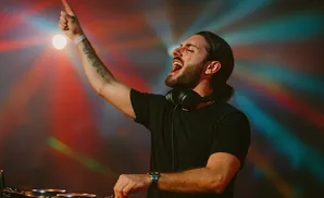 DJ with headphones, raised arm, and open mouth, performing with colorful stage lights.