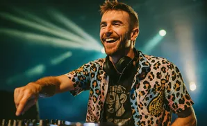 A smiling DJ in a colorful leopard print shirt plays music on a DJ booth.