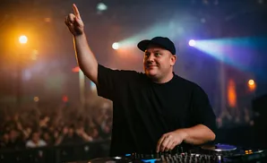 DJ with arm raised and hand pointing up, performing at a concert.