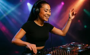 A female DJ in headphones smiles as she mixes music on a DJ setup.