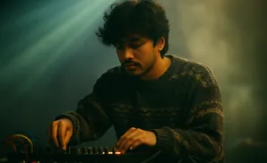 Young man with curly hair wearing a patterned sweater, focused on adjusting knobs on a soundboard.